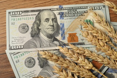 Dollar banknotes and wheat ears on wooden table, top view. Agricultural business