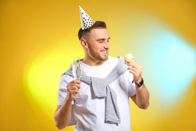 Portrait of happy man with champagne in glass and tasty cupcake on color background