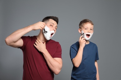 Dad shaving and son imitating him on grey background