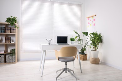 Stylish workplace with desk, chair, bookcase and potted plants at home