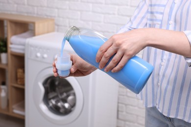 Woman pouring fabric softener from bottle into cap for washing clothes indoors, closeup