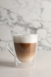 Photo of Glass cup of delicious layered coffee on white table against marble background, space for text