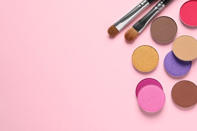 Photo of Different beautiful eye shadows and makeup brushes on pink background, flat lay. Space for text