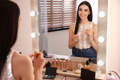 Beautiful young woman applying makeup near mirror in dressing room