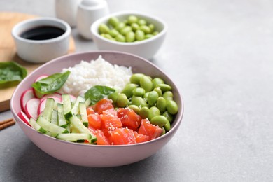 Poke bowl with salmon, edamame beans and vegetables on light grey table, space for text