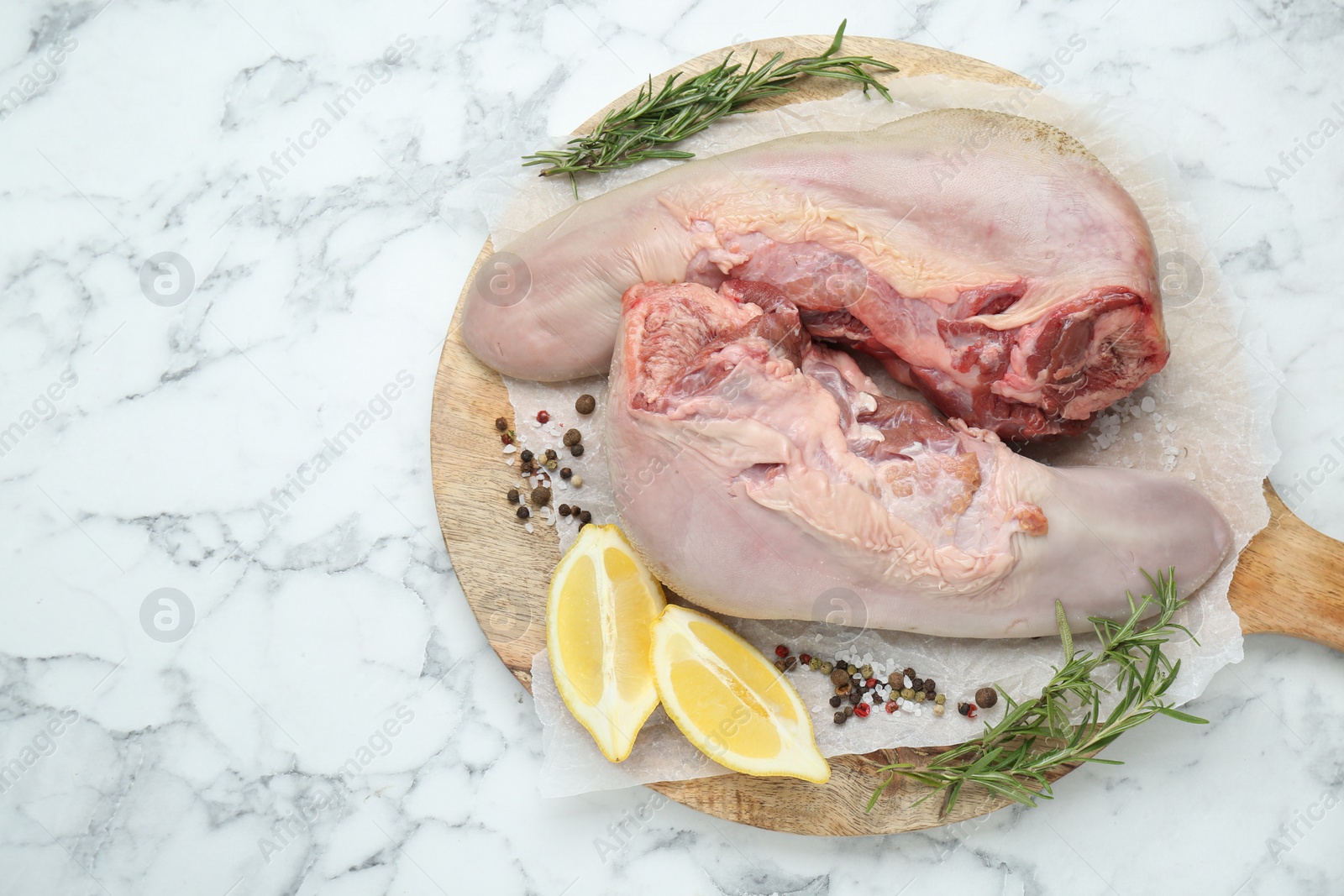 Photo of Raw beef tongues, peppercorns, salt, rosemary and lemon on white marble table, top view