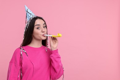 Woman in party hat with blower on pink background, space for text