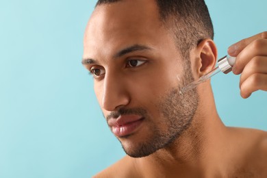 Photo of Handsome man applying cosmetic serum onto face on light blue background, closeup. Space for text