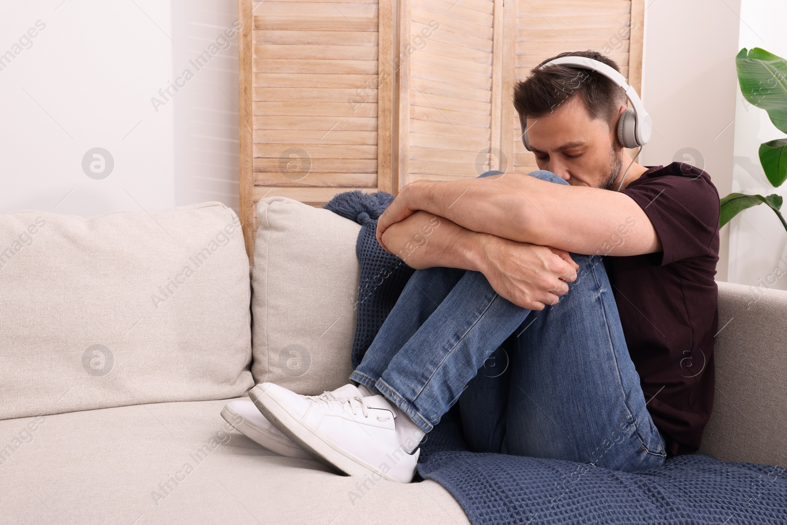 Photo of Upset man listening to music through headphones on sofa at home. Loneliness concept