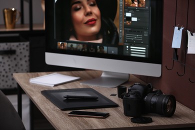 Retoucher's workplace. Computer with photo editor application, camera, smartphone and graphic tablet on table indoors