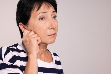 Photo of Senior woman suffering from ear pain on light grey background, closeup. Space for text
