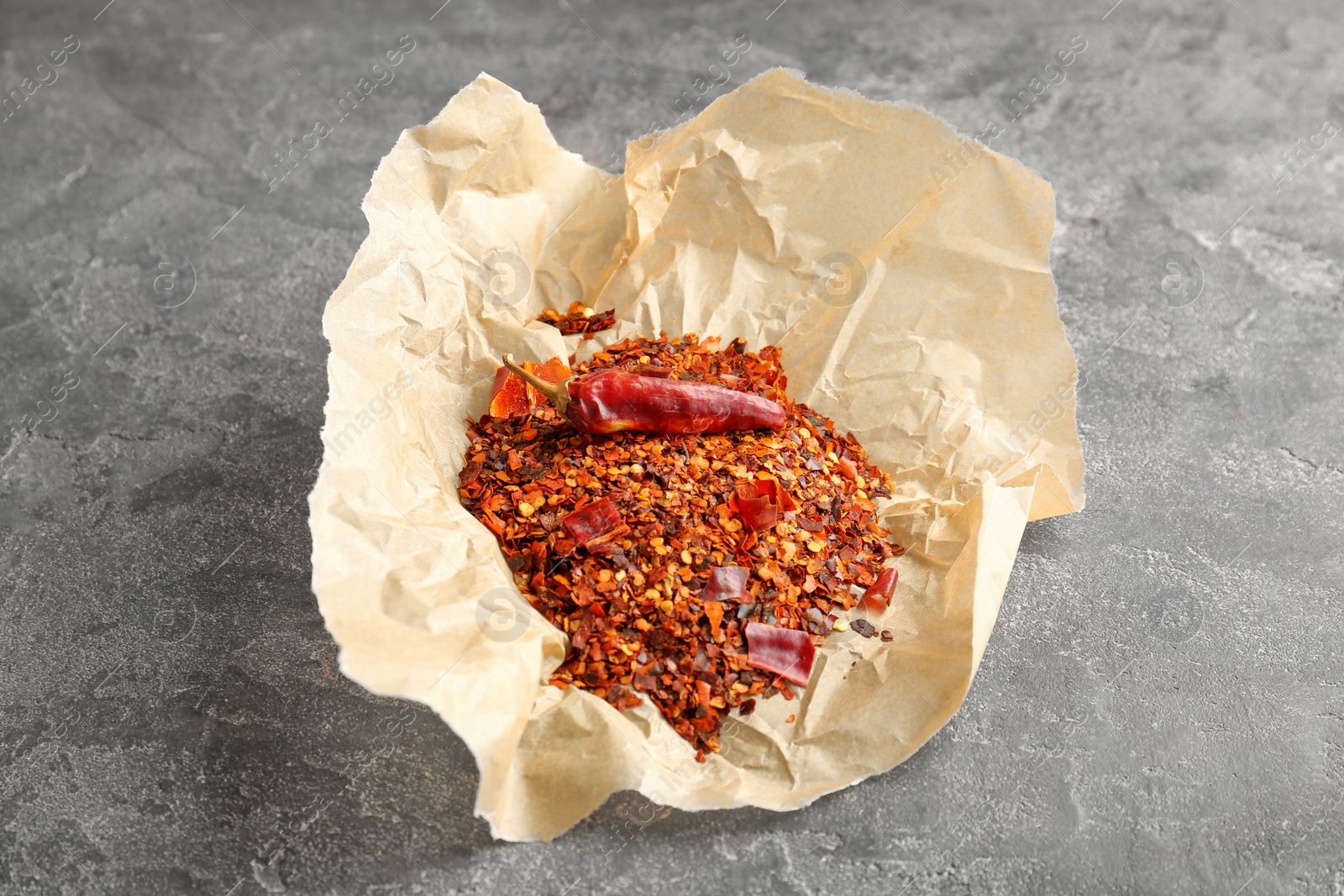 Photo of Parchment with crushed chili pepper and pod on grey background