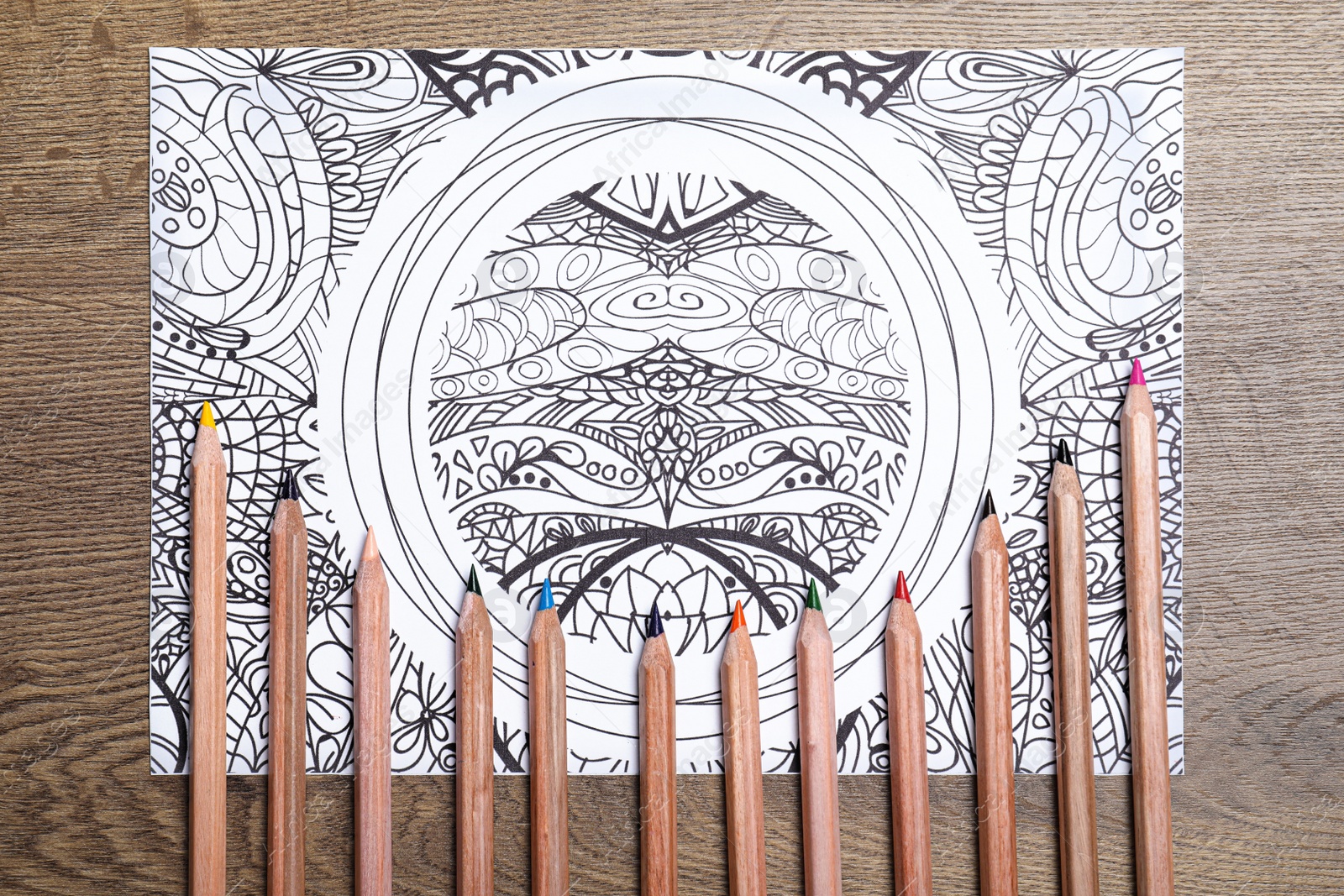 Photo of Antistress coloring page and pencils on wooden table, flat lay