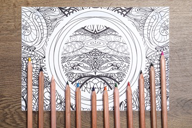 Photo of Antistress coloring page and pencils on wooden table, flat lay