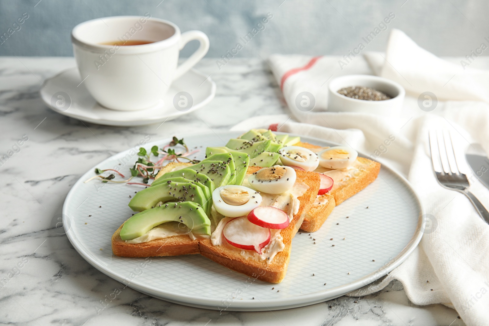 Photo of Plate of tasty toasts with avocado, quail eggs and chia seeds on marble table