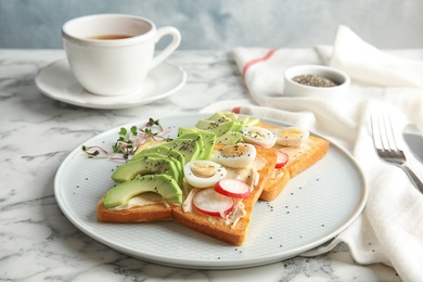 Photo of Plate of tasty toasts with avocado, quail eggs and chia seeds on marble table