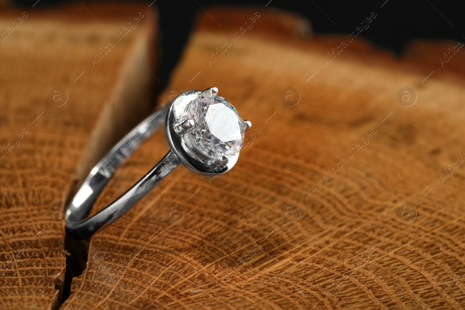 Photo of Beautiful luxury engagement ring with gemstone on tree stump, closeup