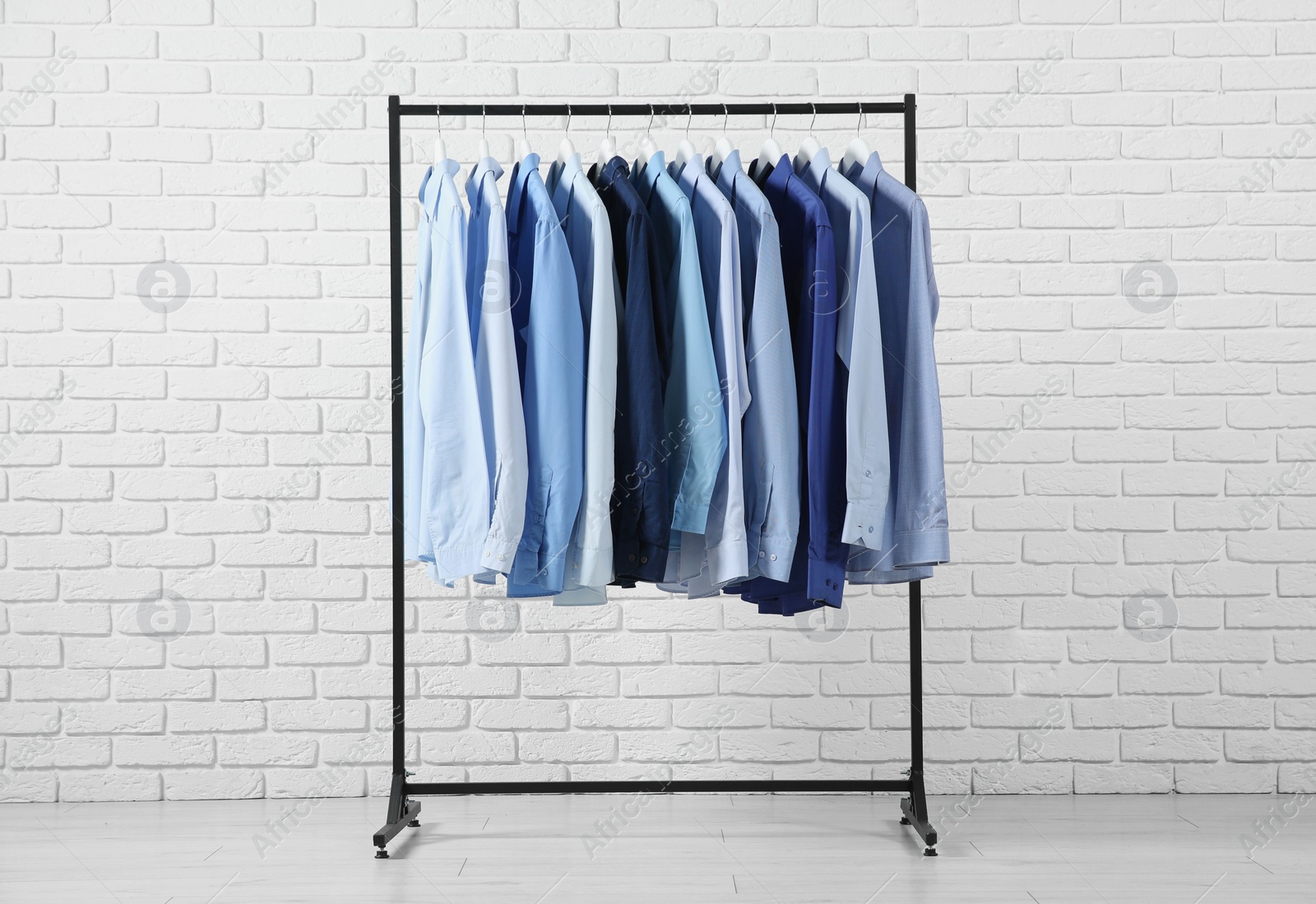 Photo of Dry-cleaning service. Many different clothes hanging on rack near white brick wall