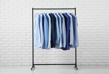 Photo of Dry-cleaning service. Many different clothes hanging on rack near white brick wall