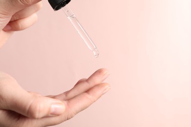 Photo of Woman applying cosmetic serum onto fingers on light pink background, closeup. Space for text