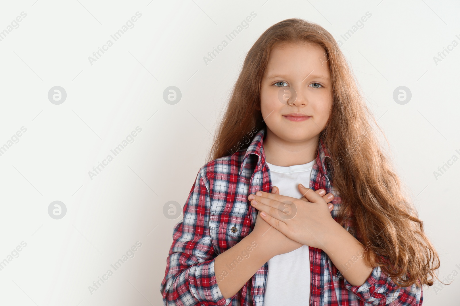 Photo of Cute grateful little girl with hands on chest against light background