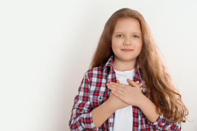 Photo of Cute grateful little girl with hands on chest against light background