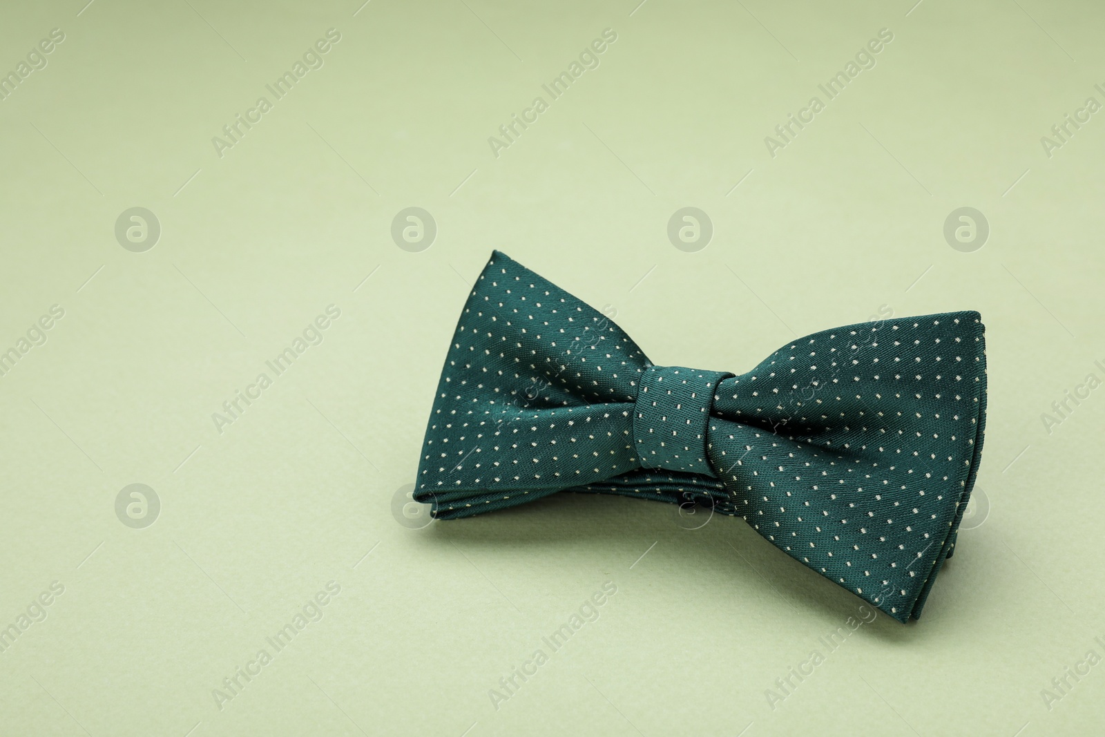 Photo of Stylish bow tie with polka dot pattern on pale green background, space for text