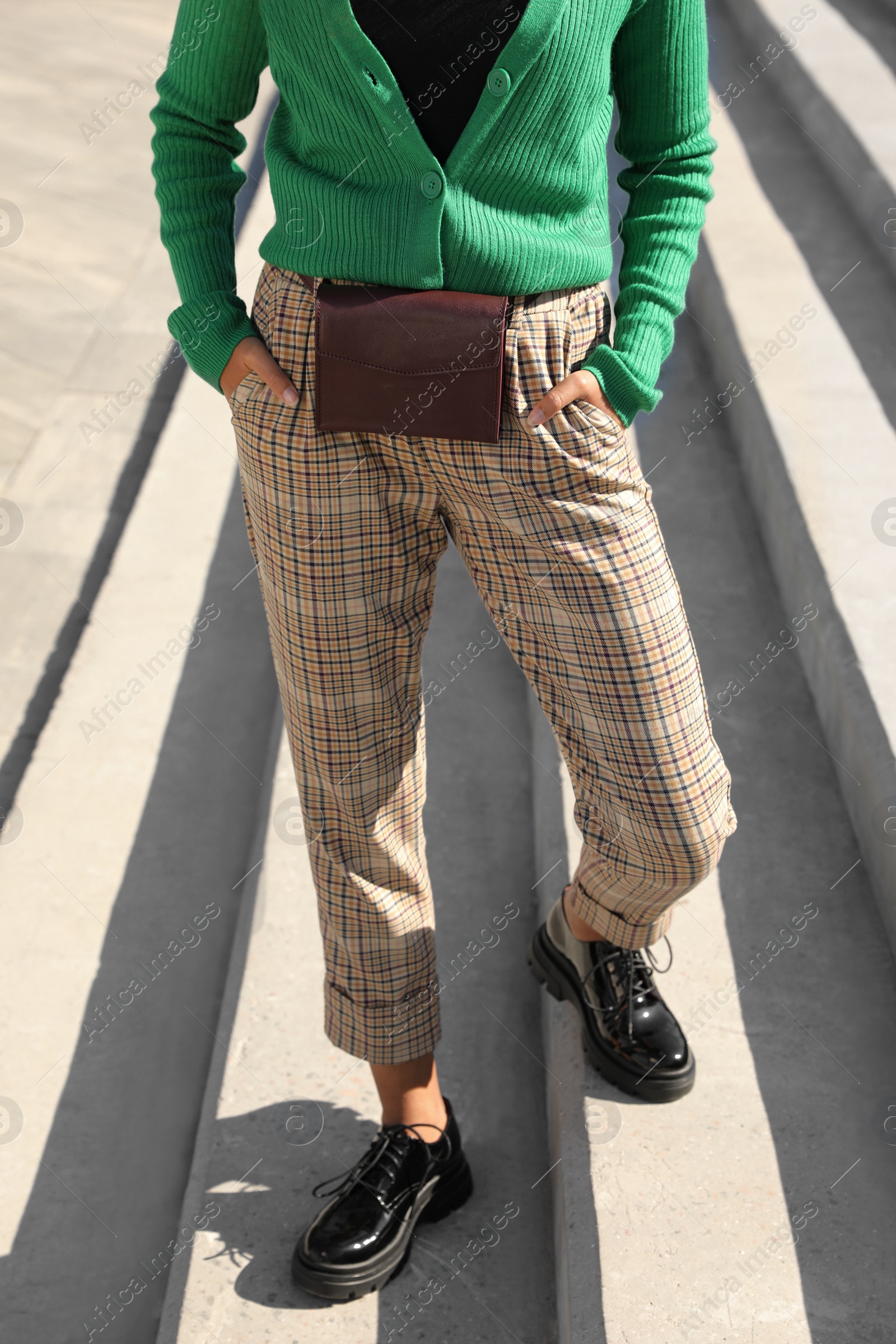 Photo of Young African American woman with stylish waist bag on stairs outdoors, closeup