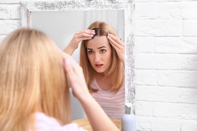 Young woman with hair loss problem near mirror indoors