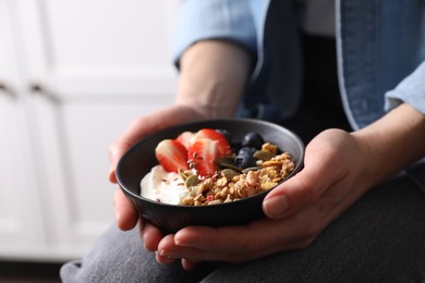 Woman holding bowl of tasty granola with berries, yogurt and seeds indoors, closeup