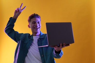 Young man with laptop talking via video chat on yellow background