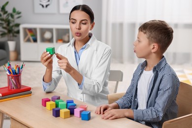 Photo of Dyslexia treatment. Therapist holding cube while working with boy at table in room