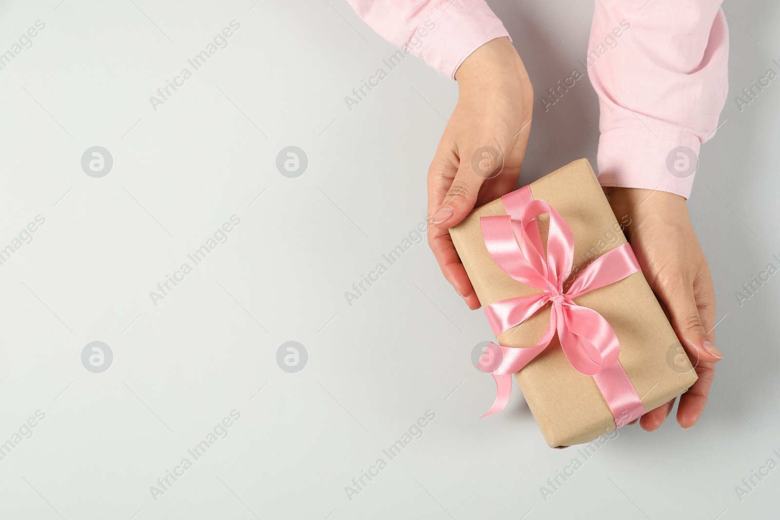 Photo of Woman holding gift box on light background, top view. Space for text