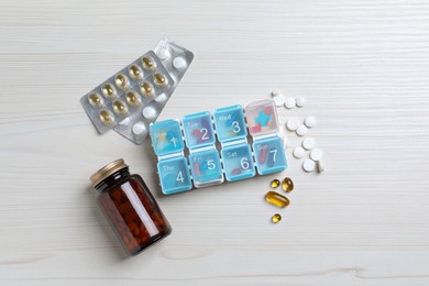 Photo of Weekly pill box and bottle with medicaments on white wooden table, flat lay
