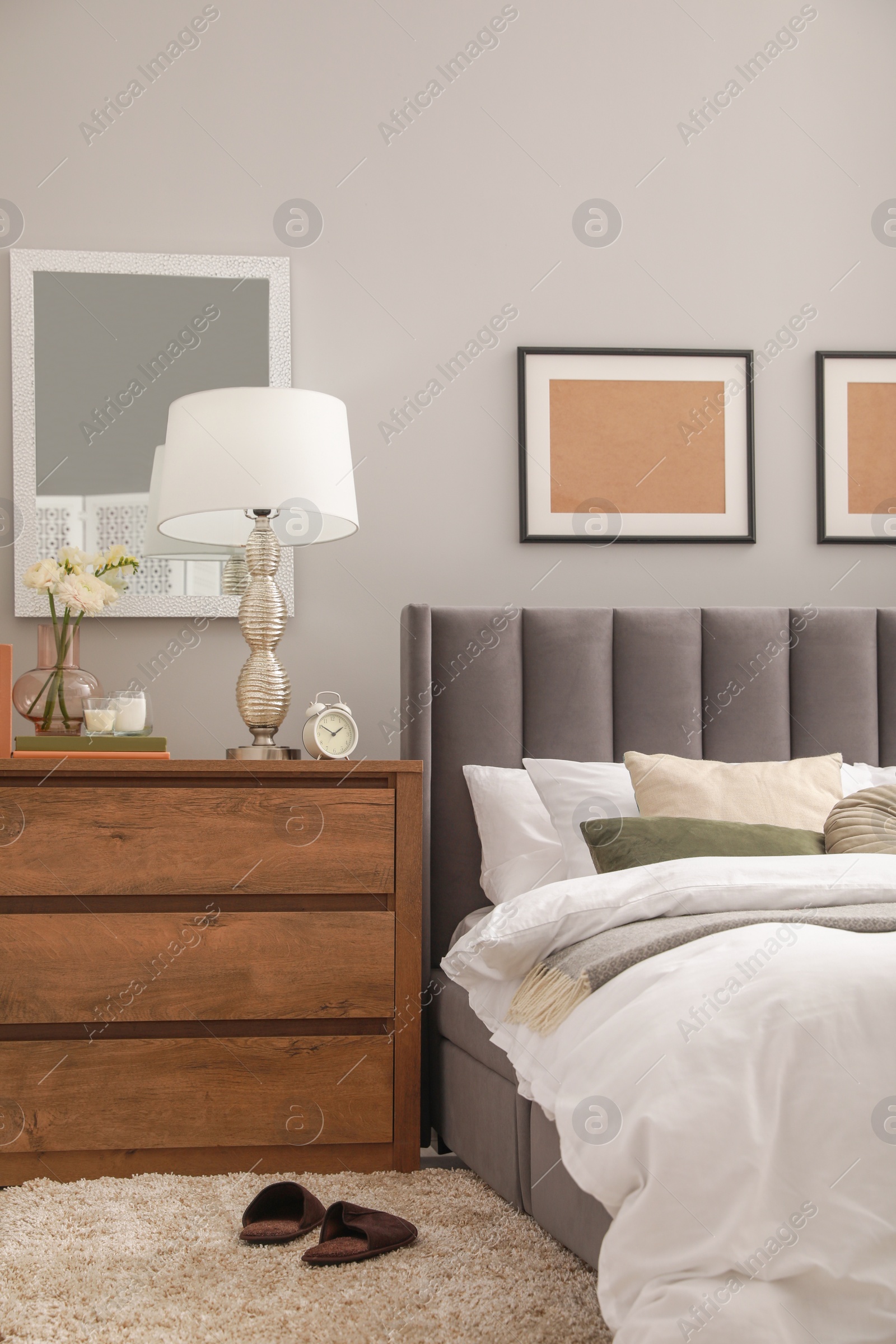 Photo of Comfortable bed with cushions, lamp and different decor on wooden chest of drawers in room. Stylish interior