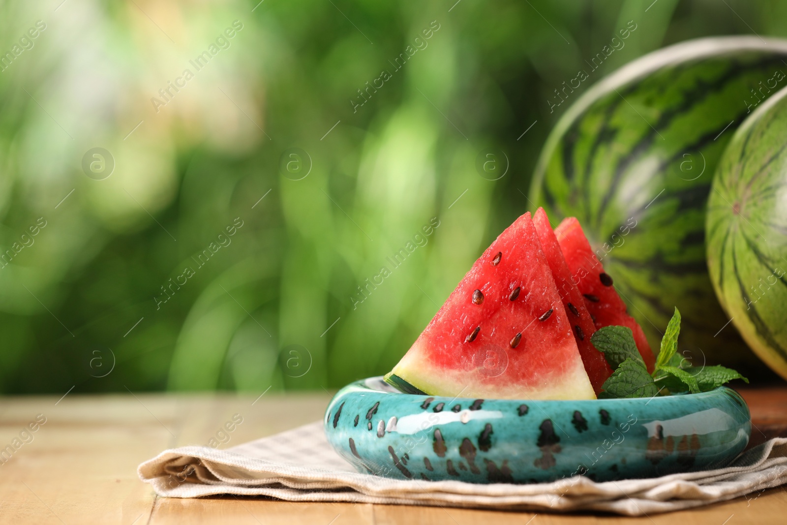 Photo of Slices of delicious ripe watermelon on wooden table outdoors, space for text