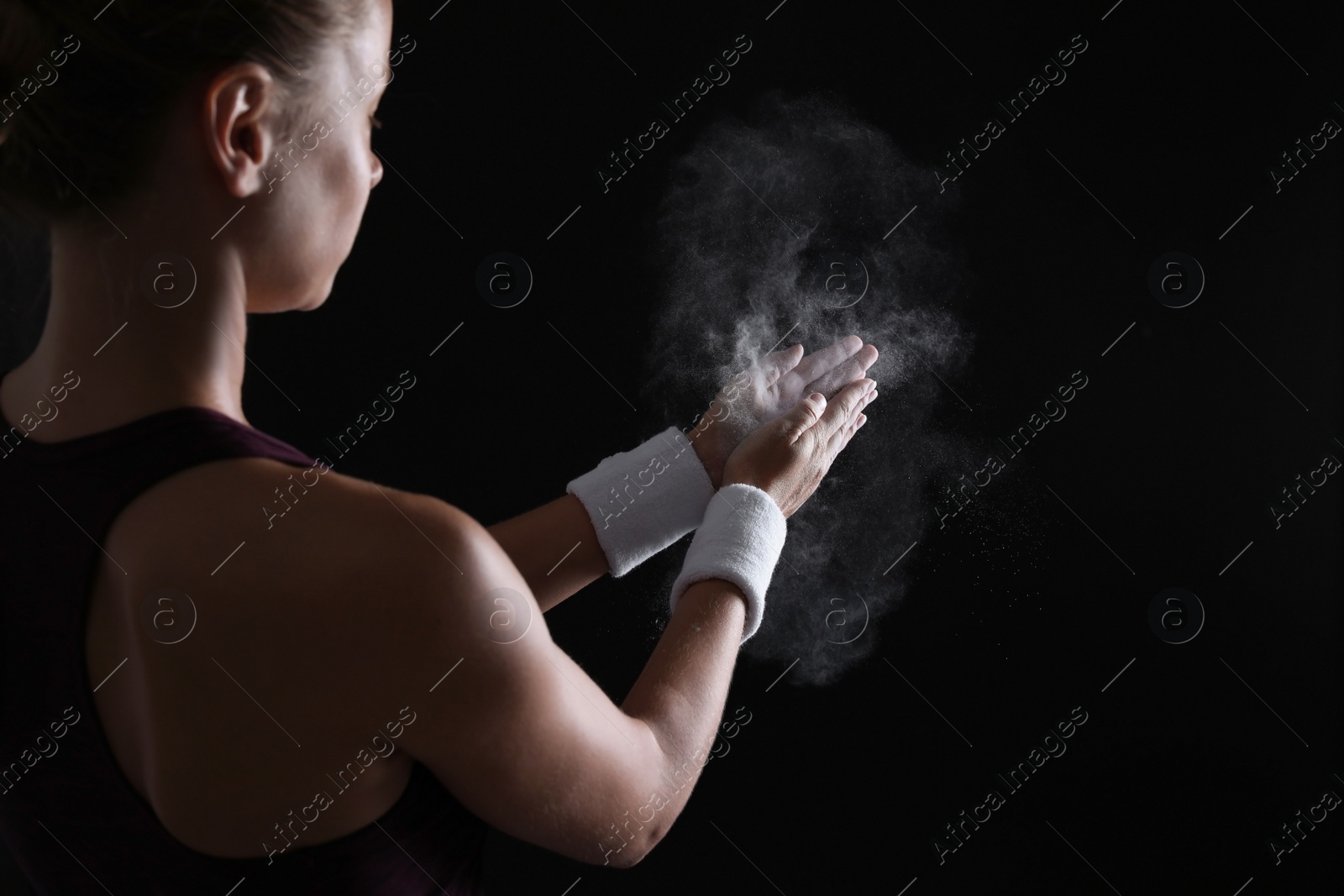 Photo of Young woman applying chalk powder on hands against dark background