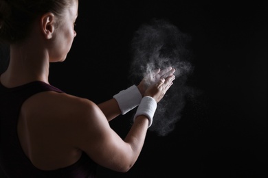 Photo of Young woman applying chalk powder on hands against dark background