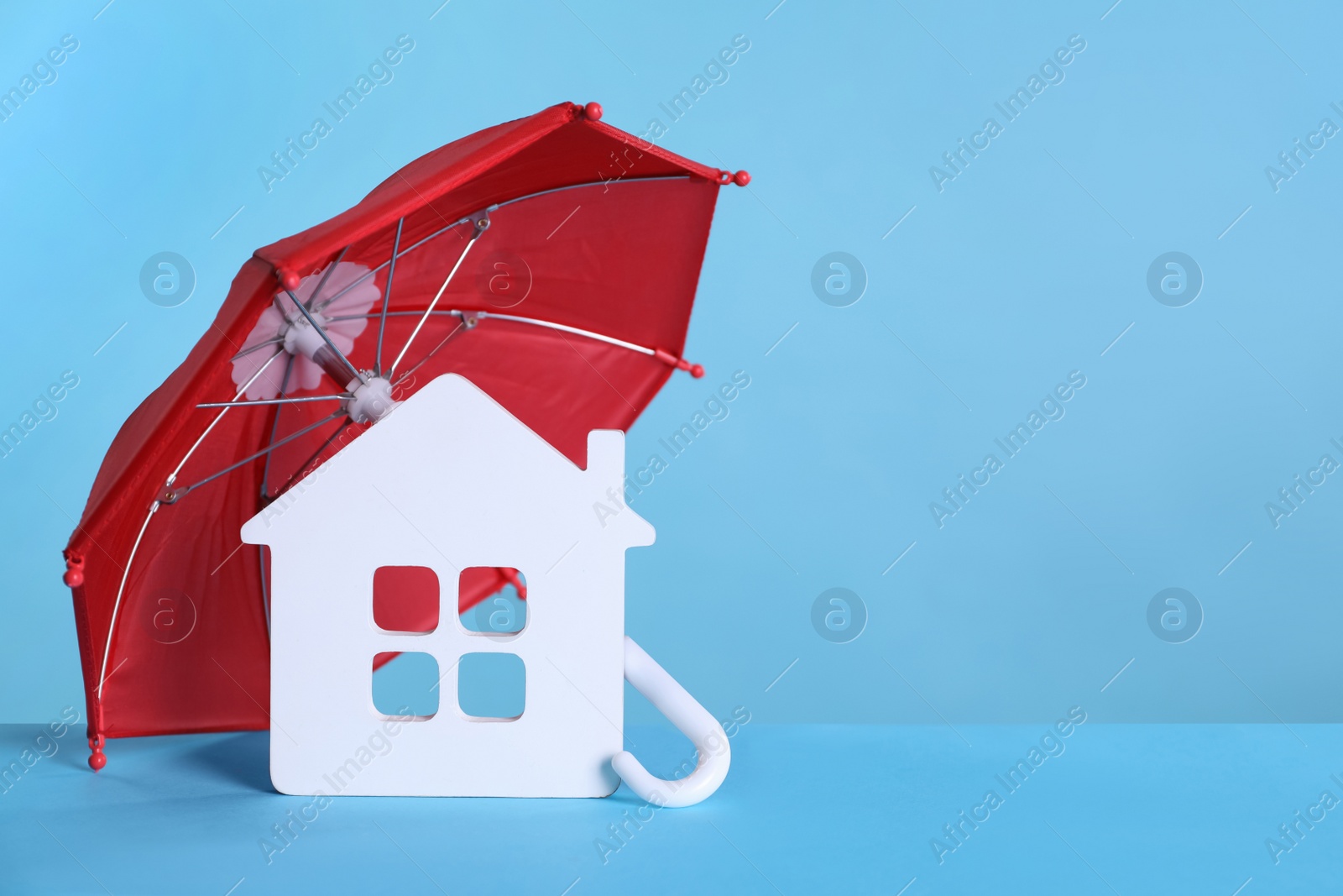 Photo of Small umbrella and house figure on light blue background. Space for text