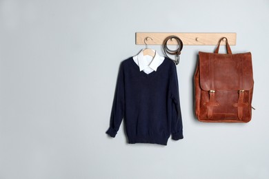 Shirt, jumper and bag hanging on white wall. School uniform. Space for text