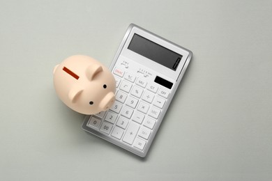 Photo of Calculator and piggy bank on light grey background, top view