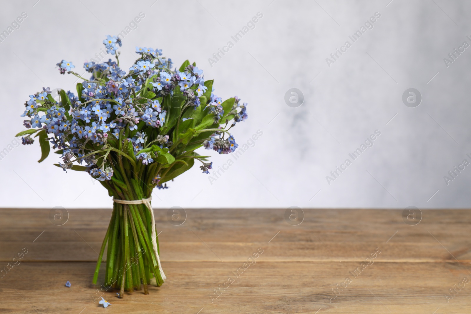 Photo of Bouquet of beautiful forget-me-not flowers on wooden table against light background, space for text