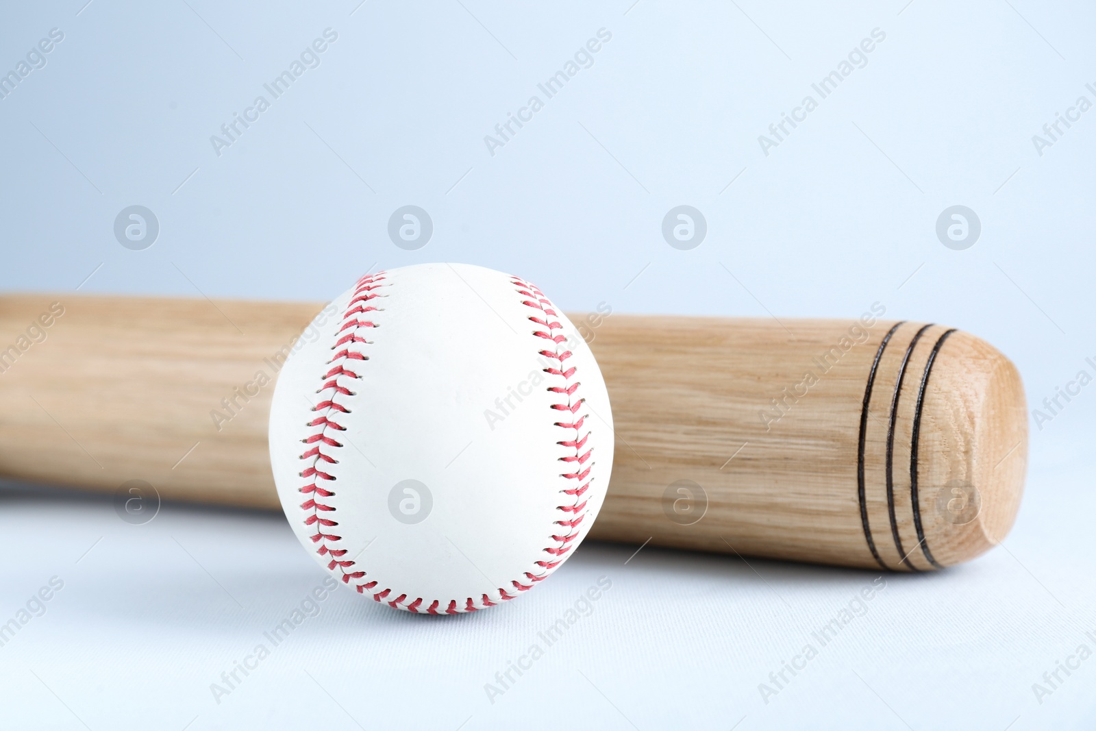 Photo of Wooden baseball bat and ball on light grey background, closeup. Sports equipment