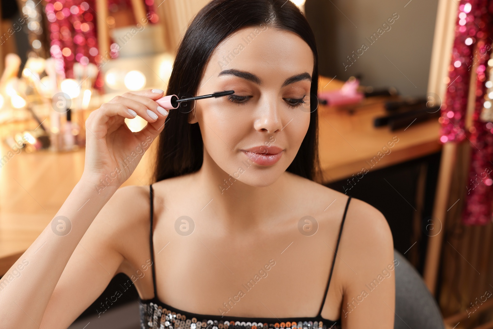 Photo of Beautiful young woman applying mascara in dressing room, closeup