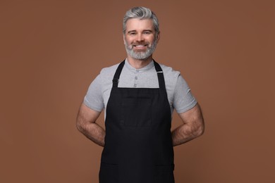 Photo of Happy man wearing kitchen apron on brown background. Mockup for design