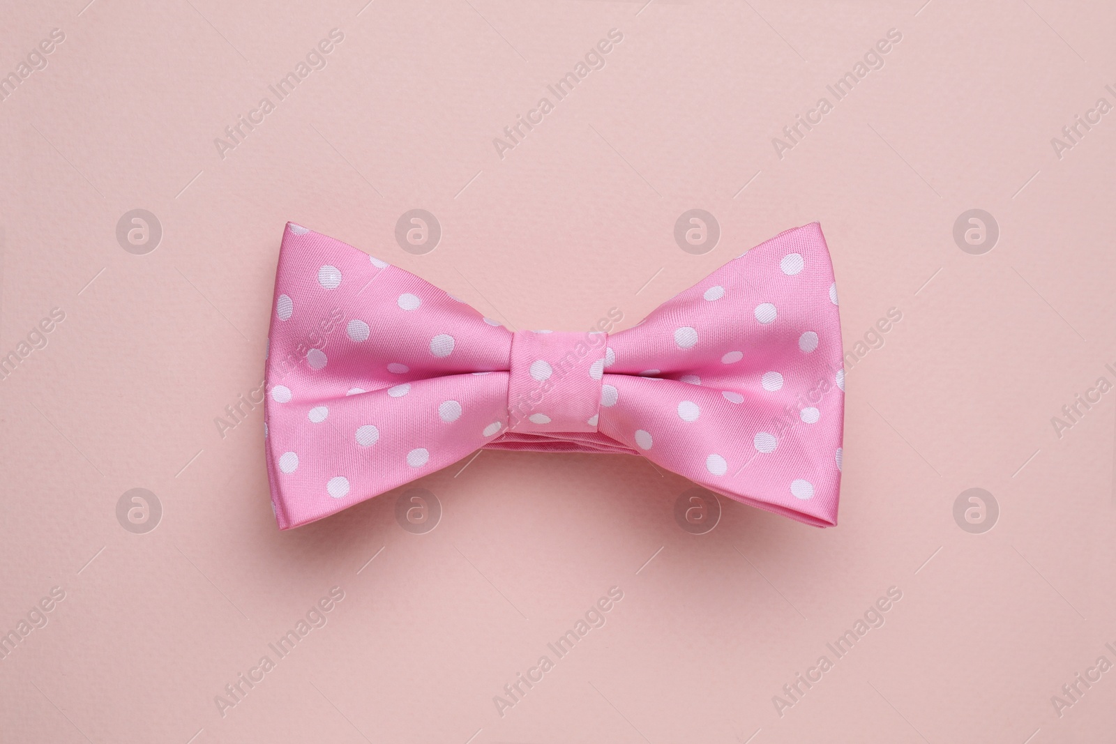 Photo of Stylish pink bow tie with polka dot pattern on beige background, top view