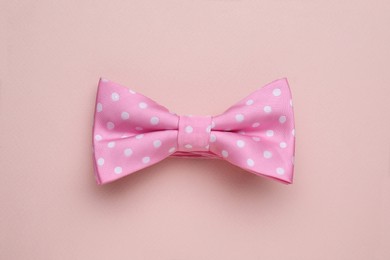 Stylish pink bow tie with polka dot pattern on beige background, top view