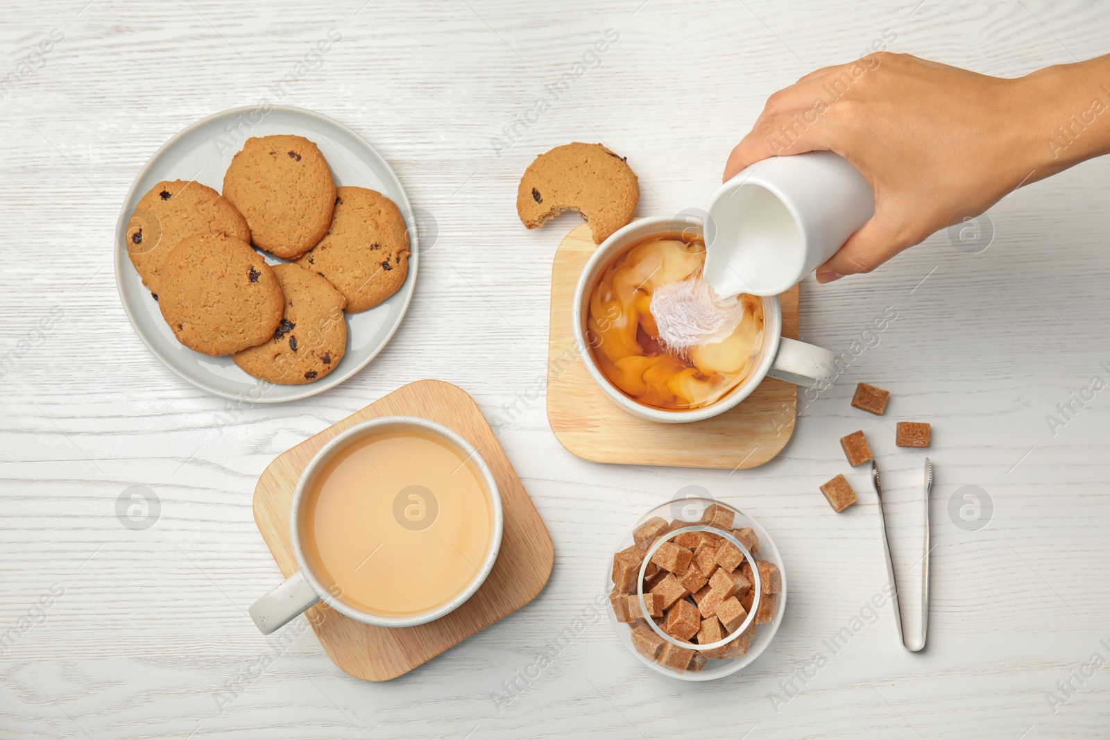 Photo of Woman pouring milk into cup with black tea on wooden table, top view