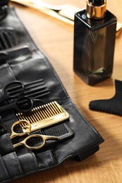 Photo of Hairdresser tools. Professional scissors and combs in leather organizer on wooden table, closeup