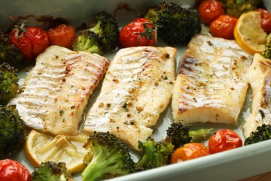 Photo of Pieces of delicious baked cod with vegetables and spices in dish, closeup